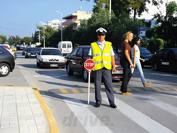 Εικόνα που συνοδεύει την ερώτηση: Στο δρόμο που κινείσθε βλέπετε τον εθελοντή σχολικό τροχονόμο να είναι σε αυτήν τη θέση. Τι θα κάνετε: